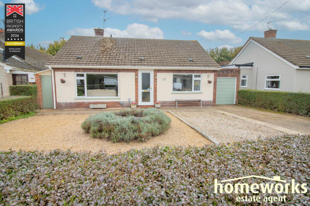 Front view of a single-story house with a gravel driveway and small shrubs. Award badge on the top left and estate agent logo on the bottom right. Bright, cloudy sky in the background.